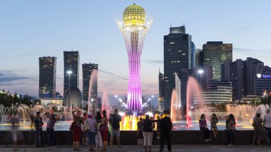 Bayterek Tower and fountain show day to night transition timelapse. People walking around. Skyscrapers on background. Bayterek is monument and observation tower in Astana. Nur-Sultan city, Kazakhstan clipart