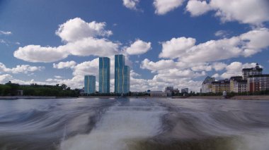 Astana, Kazakistan. Keyif teknesinden Astana 'da Ishim nehrinde hareketli bir seyahat görüntüsü. Mavi gökyüzü ve bulutlarla dolu bir yaz gününde. Bulanık hareket