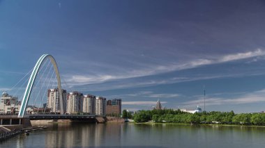 Ishim 'in üzerindeki köprüde park zamanı ve arkaplanda bulutlar var. Şehir silüeti. Orta Asya, Nur-Sultan şehri, Kazakistan