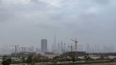 Skyline of construction cranes tower with skyscrapers on background in the Middle East day to night transition timelapse, Dubai. Evening mist. Cloudy sky clipart