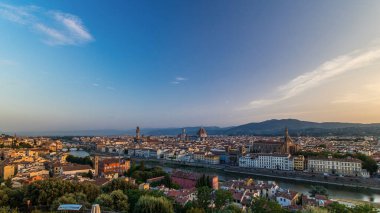Floransa şehrinin gündoğumundaki panoramik zaman çizelgesinin en üst görüntüsü. Arno nehir köprüleri ve tarihi binalar, arka planda dağlar. Yeşil ağaçlar, yaz gününde mavi bulutlu gökyüzü