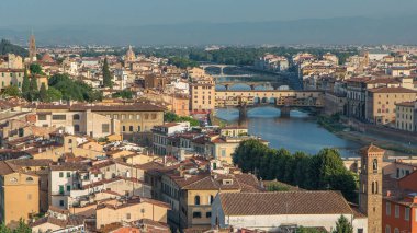 Arno nehir köprüleri ve tarihi binalar, arka planda dağlar ile gün doğumunda Floransa şehrinin en iyi hava manzarası. Yeşil ağaçlar, yaz gününde mavi bulutlu gökyüzü