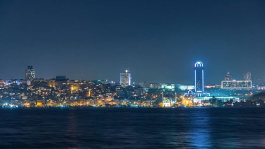 Night timelapse view of besiktas district with some illuminated skyscrapers and mosque in Istanbul taken from asian part of the city. Reflection on Bosphorus water
