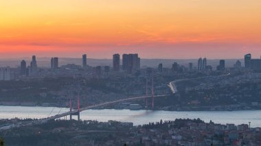 İstanbul kenti, Camlica Tepesi 'ndeki Bosphorus Köprüsü' nün (15 Temmuz Şehitleri) ve finans merkezinin havadan görünüşü günden geceye ufuk çizgisine bakıyor. Köprüde trafik ve Boğaz 'da gemi.
