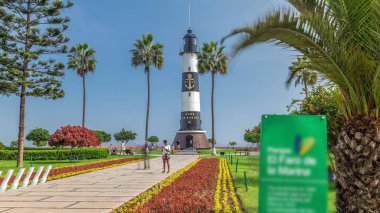 Miraflores Aşkı Parkı 'ndaki deniz feneri anıtı zaman atlaması. Çiçekli ve palmiyeli yeşil çimenler. Güneşli bir günde sahil şeridi parkı. Lima, Peru