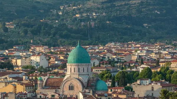 stock image Synagogue of Florence timelapse with green copper dome rising above surrounding suburban housing with green hillside behind. Aerial top view from Michelangelo square viewpoint before sunset