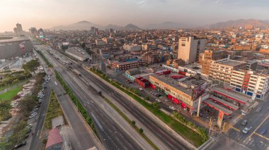 Via Expresa otoyolu ve Peru Ulusal Stadyumu yakınlarındaki gün batımı saatinde trafiği olan metropolitan otobüsünün hava manzarası. Evler ve şehrin arka planında dağlar olan silueti. Lima, Peru