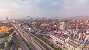 Via Expresa otobanı ve metropolitan otobüsü, Peru Ulusal Stadyumu yakınlarında her gün ve her gece hava manzaralı. Aydınlanmış evler ve arka planda dağlar olan şehir silueti. Lima, Peru