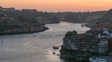 Day to night transition aerial view of the historic city of Porto, Portugal panoramic timelapse from the Dom Luiz bridge. Illuminated waterfront and curved river from above