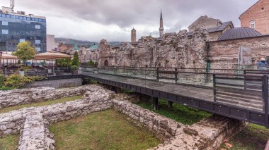 Tarihsel Taslihan, arka plandaki Gazi Husrev camii, Saraybosna ve Bosna-Hersek 'in eski gözlem kulesi ve minaresiyle birlikte zaman kayalıklarını yıkıyor. Ayak köprüsü ve duvar