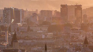Bosna-Hersek 'in tarihi Saraybosna şehir merkezinin panoramik hava manzarası, gün batımından önce ünlü binalar ve turuncu sislerle dolu