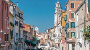 A view of Venice from above timelapse: canal, bridge, boats and an old tower in the background. Blue sky at summer day. People walking around