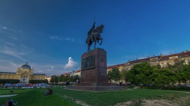 Monument of the Croatian King Tomislav timelapse hyperlapse and art pavilion in colorful park, in Zagreb, capital of Croatia. Blue cloudy sky before sunset. Panoramic view