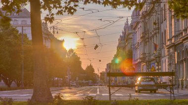 Street with sunset in the Croatian capital Zagreb. People sitting on the bench near tree. Road traffic and tram rails