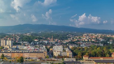 Hırvatistan 'ın Zagreb kentinin şehir merkezinin modern ve tarihi binaları ve arka planında dağlar bulunan hava manzarası. Bulutlu mavi gökyüzü ile gökdelenden üst görünüm