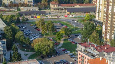 Cars moving on parking lot timelapse with green trees, lawn and residential buildings. Top view from skyscraper rooftop. Croatia, Zagreb