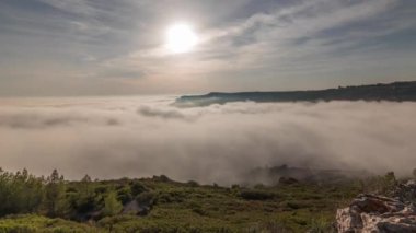 Panorama, Portekiz 'deki Sesimbra Town ve Port' un sisli zaman dilimi ile kaplı hava görüntüsünü gösteriyor. Bulutların tepesindeki manzara ve batan güneş. Setubal ilçesinde tatil köyü