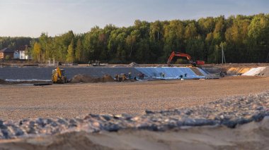 Panoramik manzara kazıcılar ve buldozerlerle şehir alanına dönüşür. Büyük bir tarladaki yeni kır köyü için şantiye manzarası. Yeşil orman ve mavi gökyüzü