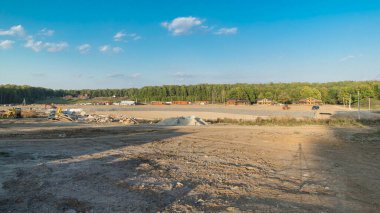 Panoramik peyzaj, mekanik zaman ayarlı kentsel alana dönüşür. Büyük bir tarlada ahşap evleri olan yeni kır köyü için şantiye manzarası. Mavi gökyüzünde güzel bulutlar