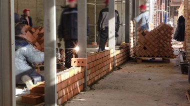 Bricklayers laying bricks to make a walls timelapse and welders weld fittings in reinforcement. Professional construction worker laying bricks and building inside in industrial site.