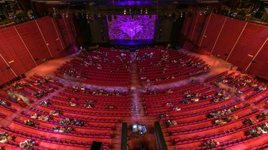 Spectators gather in the auditorium and watch the show in theatre timelapse. Large hall with red armchairs seats. Viewers filling places until turn off the light. Top view from above