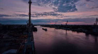 Shipyard with historical cranes in the industrial part on a riverside during sunrise aerial timelapse. Plants and factories around. Colorful sky at the morning