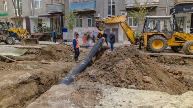 Kamu projeleri için su tedarik borusunun değiştirildiği boru hattı şantiyesinde çalışan kazıcı. Metal bir ipte boru kaldırma