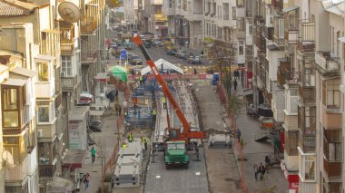 Yol inşaatında ve tramvay raylarında vinç üzerinden beton plakaları boşaltıyorum. Zaman ayarlı. Şapkalı ve üniformalı endüstriyel işçiler. Yukarıdan hava üstü görünümü