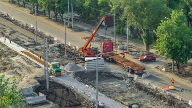 Turuncu inşaat teleskopik mobil vinç kamyon hava zaman tünelinden tramvay raylarını boşaltıyor. Şapkalı ve üniformalı endüstriyel işçiler. Şehir caddesindeki tramvay raylarının yeniden inşası