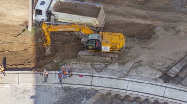 Endüstriyel kamyon yükleme kazıcısının yer değiştirmesini ve yol inşaatındaki bir çöp kamyonuna yüklenmesini yakından izleyin. Tramvay raylarının yeniden inşasının havadan görüntüsü