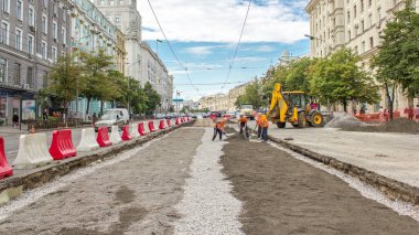 Buldozer hareket eder ve zamanı gelince toprağı ve molozu yayar. Tramvay raylarının yeniden inşasında turuncu üniformalı işçiler. Sokakta trafik vardı. Yol yapım aşamasında.
