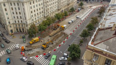 Turuncu inşaat teleskopik vinç eski tramvay raylarını kamyon saatine yüklüyor. Şapkalı ve üniformalı endüstriyel işçiler. Şehir caddesindeki tramvay raylarının yeniden inşası
