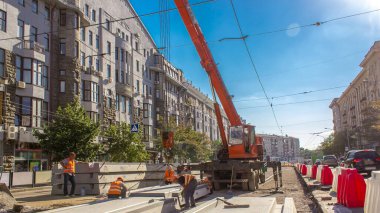 Yol inşaatı zamanına vinçle beton plakalar yerleştiriliyor. Şapkalı ve üniformalı endüstriyel işçiler. Şehir caddesindeki tramvay raylarının yeniden inşası. Mavi açık gökyüzü