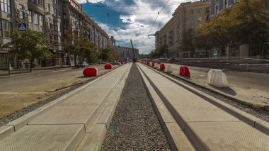 Yol inşaatı zamanına vinçle beton plakalar yerleştiriliyor. Şehir merkezinde yoğun sokak trafiği var. Şehir caddesindeki tramvay raylarının yeniden inşası
