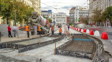 Beton, turuncu üniformalı ve mikser makineli birçok işçiyle yol inşaatı için özel plakaların yanında çalışıyor. Tramvay raylarının yeniden inşası