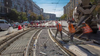 Beton döşeme ve karayolu inşaatı. Turuncu üniformalı birçok işçi ve şehir trafiği. Tramvay raylarının yeniden inşası