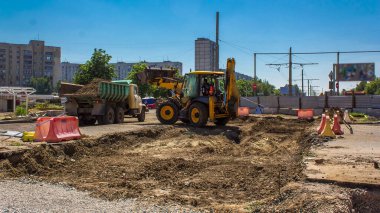 Endüstriyel kazıcı toprak kazıyor ve bir yol inşaatında bir kamyon zaman tüneline yüklüyor. Büyük bir şehirde tramvay raylarının yeniden inşasına hazırlık