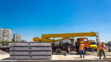 Yol inşaatı zamanında sarı vinçle beton plakaları boşaltıyorum. Şapkalı ve üniformalı endüstriyel işçiler. Şehir caddesindeki tramvay raylarının yeniden inşası