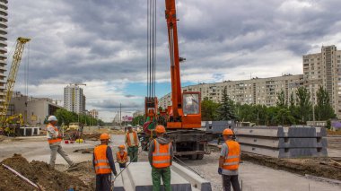 Yol inşaatında vinçle ezilmiş taşın üzerine beton plakalar yerleştiriliyor. Şapkalı ve üniformalı endüstriyel işçiler. Şehir caddesindeki tramvay raylarının yeniden inşası