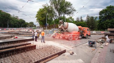 Tramvay rayları onarımı ve bakım zamanı olan bir yol inşaatı. Kavşağın ortasında beton işi ve mikser var. Demiryolu raylarının birçok işçiyle değiştirilmesi
