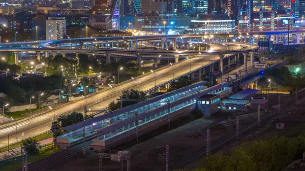 stock image Small Ring of the Moscow Railways night timelapse. Orbital railway route in Moscow, Russia. Shelepikha Station aerial top view with traffic on third transport ring and skyscrapers behind