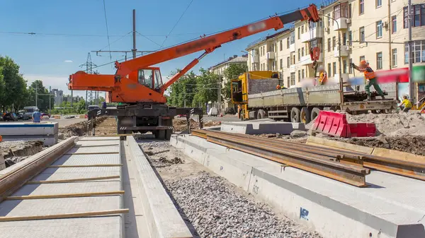 Turuncu inşaat teleskopik mobil vinç kamyondan beton plakalara giden tramvay raylarını boşaltıyor. Üniformalı sanayi işçileri. Şehir caddesindeki tramvay raylarının yeniden inşası