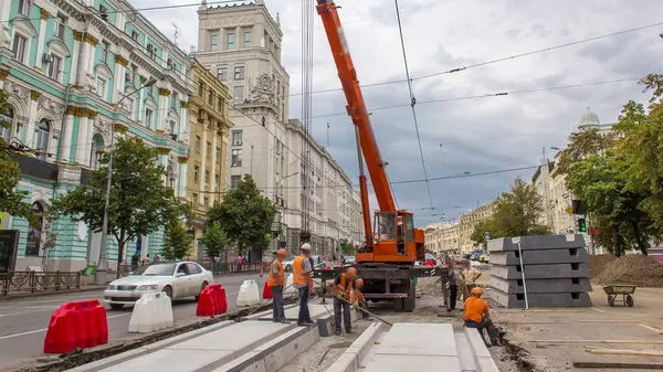 stock image Installing concrete plates by crane at road construction site timelapse. Industrial workers with hardhats and uniform. Reconstruction of tram tracks in the city street. Cloudy sky