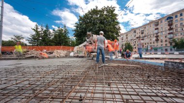 Tramvay rayları onarılan ve bakım süreleri yüksek olan yol inşaatı. Metal bir şebekeye beton dökülüyor. Kavşağın ortası. Arkaplanda yeşil ağaçlar