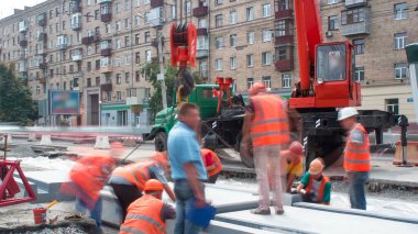 Tramvay rayları onarımı ve bakım zamanı olan bir yol inşaatı. Vinçle beton plakalar yerleştiriliyor. Kask ve üniformalı endüstriyel işçiler..