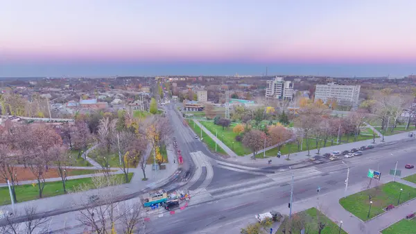 stock image Road intersection with reconstructed tram tracks aerial day to night transition. Kharkiv city from above. Tram stop and car traffic on avenue. View to the park and residential districts. Ukraine.