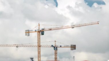 Bulutlu bir zaman dilimi olan bir bina kompleksi üzerinde çalışan ve hareket eden birkaç vinç de dahil olmak üzere büyük bir inşaat alanı. Büyük bulutlar geçip gidiyor.