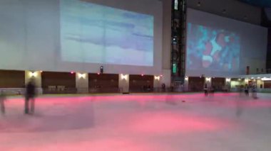 İnsanlar kapalı bir buz pateni sahasında alışveriş merkezinin renkli ışıklarıyla hipervane hızında kayıyorlar. Kış boyunca eğlenmek.