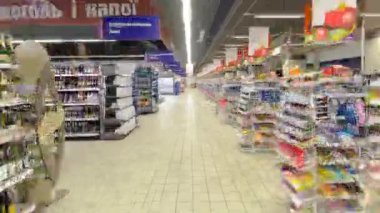 Renkli raflarla dolu bir süpermarket koridorunda yürüyün ve müşteriler zaman aşımına uğramış ürünleri seçin. Alışveriş merkezinde büyük bir hipermarket. Sağ tarafında nakit masaları olan satırları kontrol et