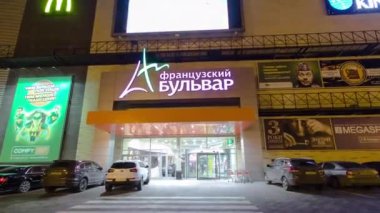 Otomatik kapıları olan ticari merkezin ana girişi gece vakti hızlandırılmış. Önünde park yeri olan büyük bir alışveriş merkezi.